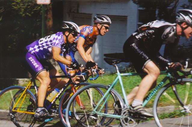 tři závodníci jedou na kole, ve fialovém dresu, v oranžovém a v černém